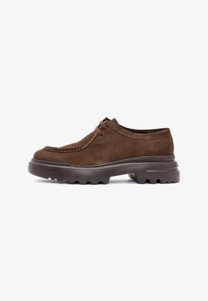 Bruine suède veterschoenen met een dikke robuuste zool en contrasterende stiksels langs de teen en zijkanten, zijaanzicht op een witte achtergrond.