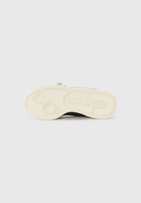Black sneaker with a textured, white rubber sole featuring a wave pattern; includes branding on the outsole. Simple, functional design.