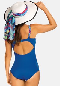 Niebieski jednoczęściowy kostium kąpielowy z odkrytymi plecami. Biały kapelusz z szerokim rondem, na którym jest związany kolorowy, wzorzysty szalik.