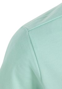 Světle mátově zelené tričko s hladkým, texturovaným bavlněným materiálem, zaobleným švem na rameni a volným střihem.