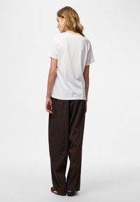 Fehér, rövid ujjú pamut póló barna csíkos, bő szárú nadrággal párosítva. A megjelenést barna balerinacipő teszi teljessé.