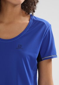 Blå sport t-shirt med rund halsringning, korta ärmar, texturerad tyg och reflekterande detaljer. Har en liten svart logotyp på bröstet.