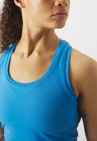 Camisola desportiva azul com decote redondo, design sem costuras e detalhes texturizados nas laterais. Visão em close que foca na parte superior do torso.