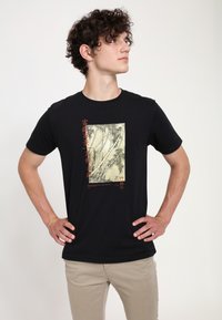 Sort bomulds t-shirt med et farverigt bambusdesign i midten og tekst i rød. Rund halsudskæring og korte ærmer.