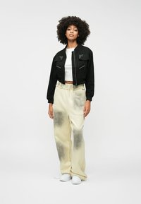 Crna skraćena jakna s detaljima od čavala, bijela majica i svijetlosmeđe hlače s tamnim gradijentom. Bijele tenisice upotpunjuju izgled.