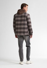 Grijs geruite flanellen shirt met een bruine capuchon binnenlaag, gecombineerd met lichtgrijze slim-fit jeans en beige sneakers.