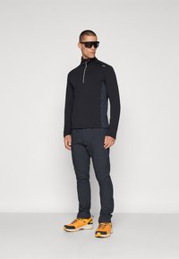 Maglione nero con zip e maniche lunghe, con pannelli laterali grigi, abbinato a pantaloni scuri e scarpe da ginnastica con accenti gialli.