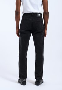 Jeans de denim negros con corte recto, que cuentan con cinco bolsillos, un parche con el logo en la cintura y detalles de costura visibles.