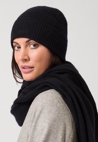 Conjunto de gorro y bufanda de punto negro, que presenta una textura acanalada con tela suave y cálida. El gorro ajusta bien y la bufanda cae de manera suelta.