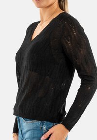 Maglione nero lavorato a maglia con scollatura a V, texture a costine e maniche lunghe. Presenta un design leggermente trasparente e una vita aderente.