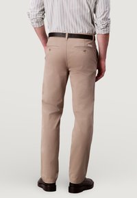 Beżowe bawełniane spodnie o prostym kroju, z dwoma tylnymi kieszeniami i brązowym paskiem. Noszone z pasiastą koszulą z długim rękawem.