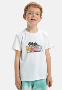 Camiseta de algodón blanca con un colorido logo de "QUIKSILVER" y gráficos de palmeras. Manga corta y cuello redondo.
