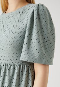 Strukturierte mintgrüne Kleid mit Chevron-Muster, kurzen Puffärmeln und einer gerafften Taille. Hergestellt aus atmungsaktivem Stoff mit Lochmuster-Details.