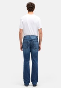 Niebieskie dżinsy z prostą nogawką, z talią o średnim stanie, dwoma tylnymi kieszeniami i subtelnym efektowaniem. Noszone z gładką białą koszulą.