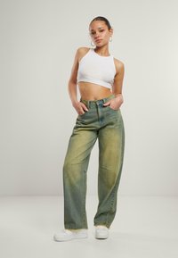Baggy, falmede grøn denimjeans med forlommer og råkant, iført en hvid ribbet crop top og hvide sneakers.