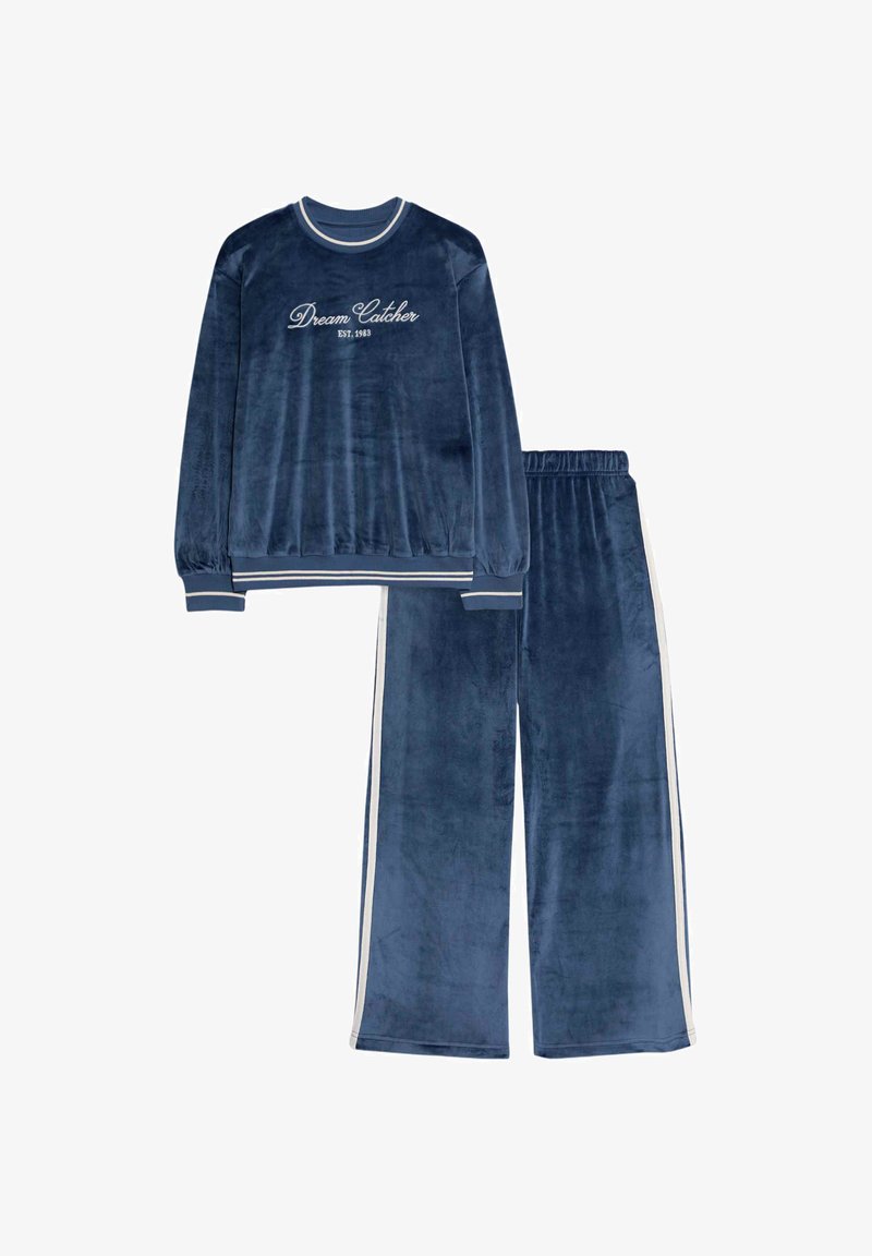Marineblauwe velours trainingspak bestaat uit een langemouwen top met de tekst "Dromen Vangen" en joggers met witte zijstrepen. Zachte textuur.