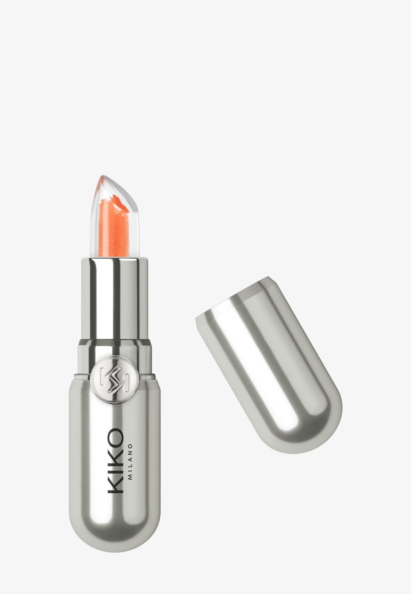 Silver lipstick tube with transparent cap showing orange lipstick inside, cap removed and placed beside the tube.