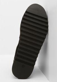 Musta kumipohja, jossa on vaakauritus pitoa varten, pyöristetty kanta ja sileä tekstuuri.