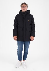 Parka negra con capucha, botones frontales y dos grandes bolsillos delanteros. El material parece resistente; cuenta con una placa de logo en el pecho.