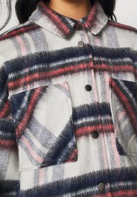 Geruite button-up shirt van zacht, gebrusht materiaal. Kenmerkt grijze, rode en marineblauwe strepen. Twee voorkruiszakken met zwarte drukknoopsluitingen.