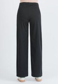 Černé široké kalhoty vyrobené z měkké tkaniny s elastickým pasem. Design zahrnuje hladkou texturu a dlouhý siluetu.