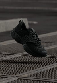 Juodos sportinės bateliai su tinklelio viršumi, tekstūruotais akcentais ir paminkštintu kraštu. Sukurti su storu padu ir ryškia raištelių sistema.