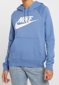 Blå sweatshirt med huva, med en stor vit Nike-logotyp på bröstet, framficka och ribbade ärm- och nederkanter. Mjuk tygtextur.