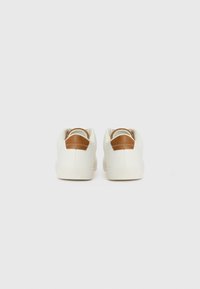 Zapatillas blancas con una textura lisa, que cuentan con un acento de talón de cuero marrón y una suela de goma con un patrón en el dibujo.