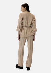 Beżowy zestaw swetra i spodni z dzianiny o prążkowanej fakturze i paskiem w talii. Długie rękawy i szerokie nogawki spodni. Czarne obuwie na platformie.