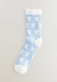 Calcetín azul claro con patrones de lazo blancos, parte superior suave y peluda, y puntera y talón blancos sólidos. Está hecho de un material texturizado y acogedor.