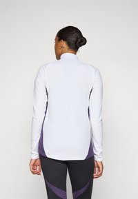Haut de sport à manches longues en blanc et violet avec un col haut, doté d'une coupe décontractée et d'accents sur les panneaux latéraux, fabriqué en tissu évacuant l'humidité.