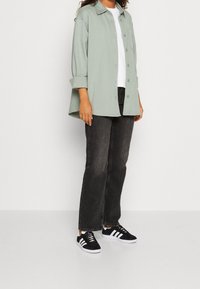 Camicia oversize verde menta con bottoni davanti, t-shirt bianca sotto, abbinata a jeans neri a vita alta e sneakers nere con strisce bianche.