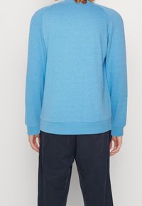 Suéter de cuello redondo azul claro con patrón texturizado, puños acanalados y dobladillo. Está hecho de una tela suave y cuenta con hombros caídos para un ajuste relajado.