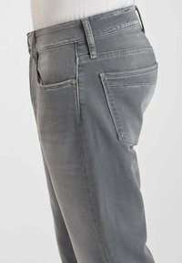 Jeans de mezclilla gris con un corte slim, que cuentan con bolsillos delanteros y traseros, detalles de costura sutiles y un cierre de botón clásico en la cintura.