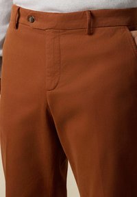 Hnědé bavlněné kalhoty se hladkým povrchem, se zapínáním na jeden knoflík, bočními kapsami a upraveným střihem.