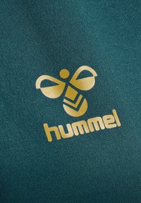 Teal stof met een gouden logo dat een gestileerde bij met een naar boven wijzende geometrische vorm weergeeft, met daaronder het woord "hummel".