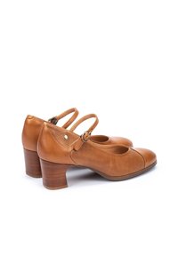 Zapatos de cuero marrón claro con punta redonda, tacón bloque de altura media y diseño perforado en los laterales. Cuentan con correas ajustables en los tobillos.