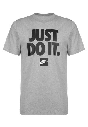 T-shirt en coton gris à manches courtes et col rond. Présente un texte noir audacieux indiquant « JUST DO IT. » et un petit logo Nike.