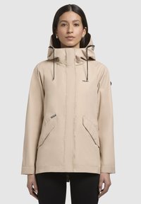 Beige waterdichte jas met een hoge kraag en verstelbare capuchon, voorzien van twee grote voorzakken en een gladde, matte textuur.