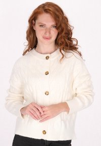 Gebreide crèmekleurige cardigan met een gestructureerd kabelpatroon, voorzien van vijf bruine knopen en ribgebreide manchetten en onderkant.