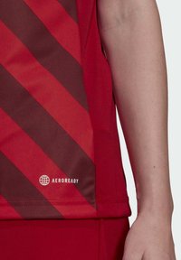 Rotes Sporttrikot mit diagonalen dunkelroten Streifen, aus atmungsaktivem Stoff; enthält ein weißes "AEROREADY"-Logo nahe dem Saum.
