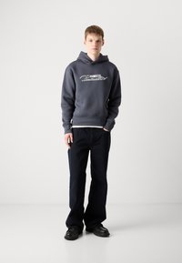 Gray hoodie with white graphic text, paired with dark blue wide-leg jeans and black shoes. The fabric appears soft and unadorned.
