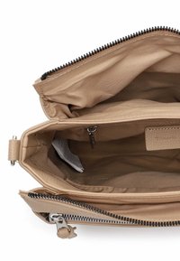 Wnętrze beżowej skórzanej torebki z zamknięciem na zamek błyskawiczny, ukazujące wiele przegródek oraz subtelny panel z teksturą. Wyściełane materiałem tkaninowym.