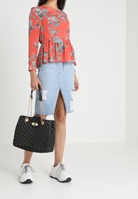 Kwiatowy top w odcieniu brzoskwiniowym z peplum w talii, jasnoniebieska spódnica dżinsowa z przetarciami i przednim rozcięciem, czarna torebka z ćwiekami oraz białe buty sportowe.