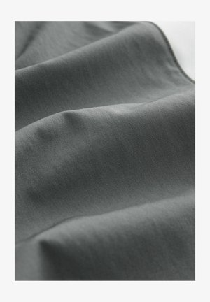 Harmaa kangas, jossa on sileä rakenne, esittelee pehmeitä taitoksia ja hienovaraisia sävyvaihteluita, mikä viittaa kevyeseen ja joustavaan materiaaliin.