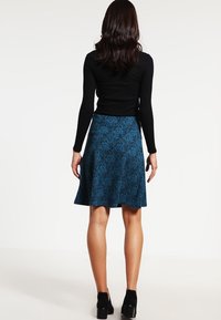 Falda de patrón floral azul con forma acampanada y textura suave, combinada con una blusa negra de manga larga de canalé y zapatos negros.