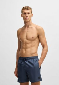 Mörkblå badshorts för män i ett lätt och slätt material med elastisk midja, dragsko och sidofickor i en minimalistisk design.