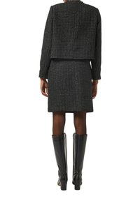 Czarna tweedowa marynarka z pasującą spódnicą, wykonaną z teksturowanej tkaniny. Dopełnieniem stylizacji są lakierowane czarne kozaki do kolan.