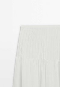 Hvid plisseret nederdel i blødt, let stof. Har en smock-skulder i taljen for en fleksibel pasform og en subtil tekstur over det hele.