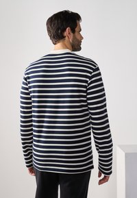 Marineblau-weißer gestreifter Langarmshirt mit Rundhalsausschnitt und lockerer Passform. Sanfter Stoff, seitliche Schlitze und kontrastierende Ärmelbündchen.